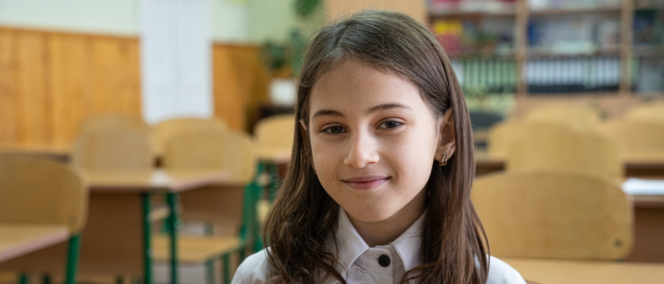 Ein junges Mädchen lächelt in einem Klassenzimmer in die Kamera