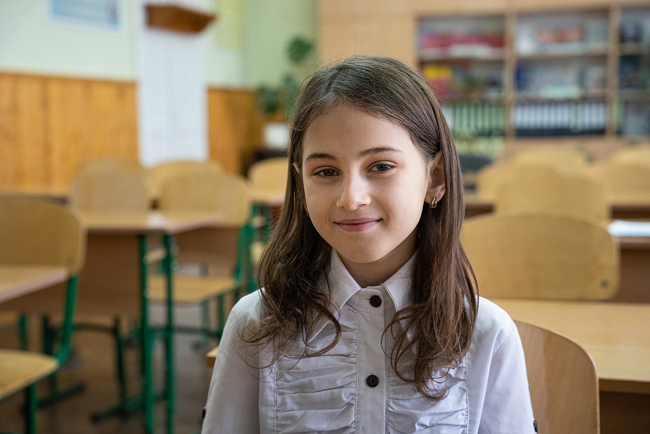Ein junges Mädchen lächelt in einem Klassenzimmer in die Kamera
