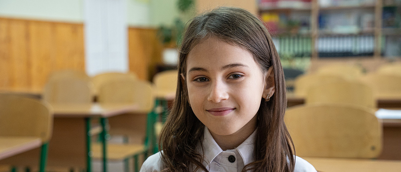 Ein junges Mädchen lächelt in einem Klassenzimmer in die Kamera