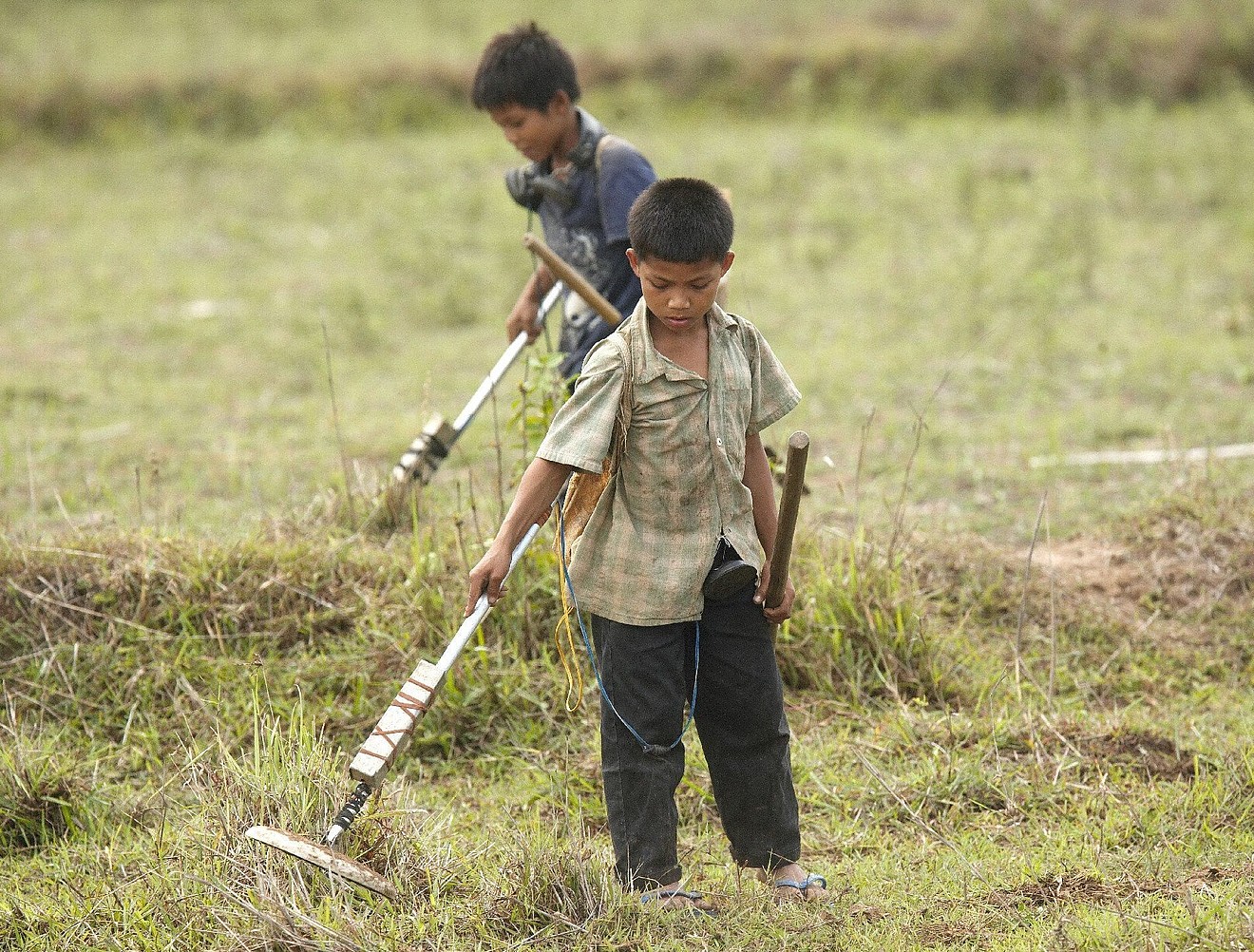 Ein Junge aus Laos sucht mit einem Detektor den Boden nach Streubomben und anderen Kriegsresten ab