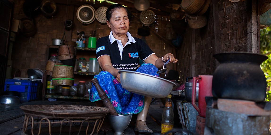 Eine Frau mit Beinprothese sitzt in ihrer Hütte und arbeitet.