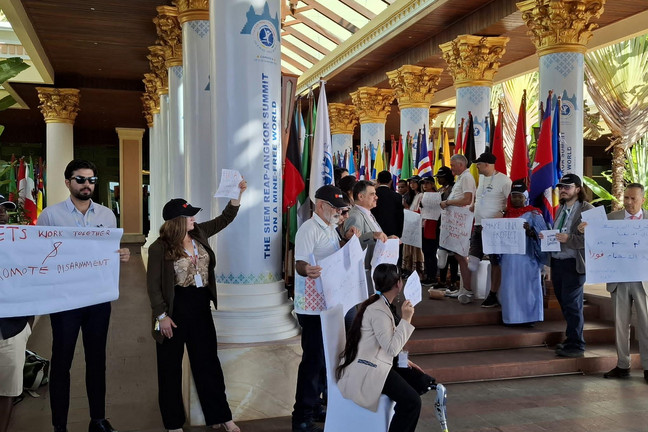 Viele Menschen mit Schildern in einem asiatischem Tempel. Ein Mann trägt eine Beinprothese.