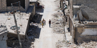 Sicht von oben auf eine zerstörte Straße. Ein paar Kinder gehen die Straße entlang.