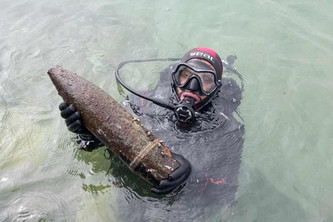 Ein Taucher hält einen Blindgänger über Wasser.
